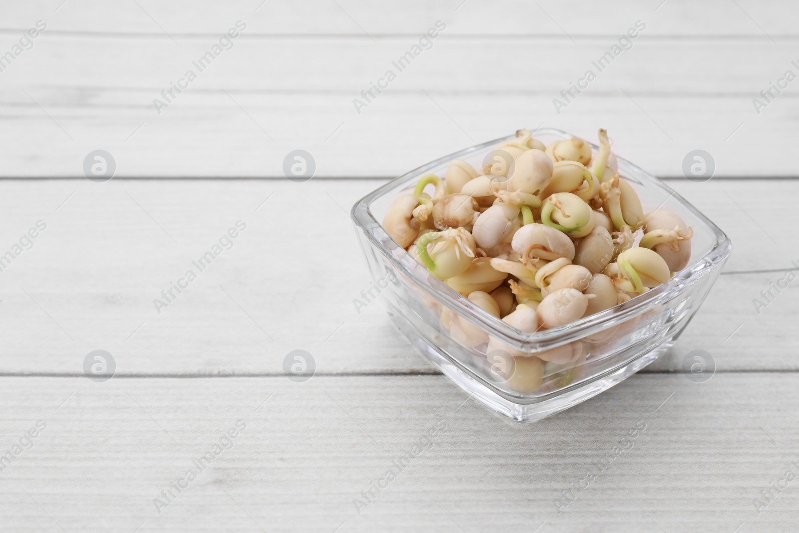 Photo of Sprouted kidney beans in bowl on white wooden table, closeup. Space for text