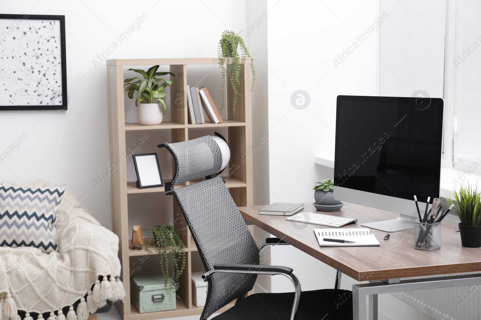 Photo of Cosy workspace with computer on desk, stylish furniture and potted plants at home