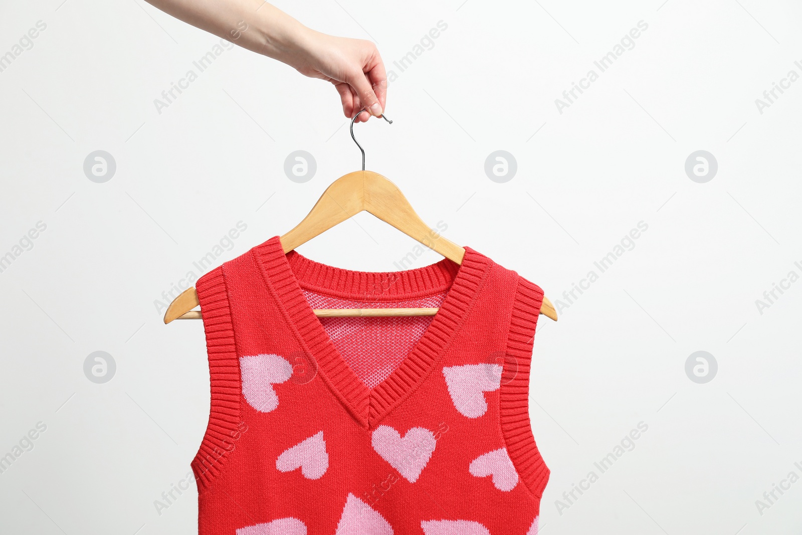 Photo of Woman holding hanger with vest near white wall, closeup