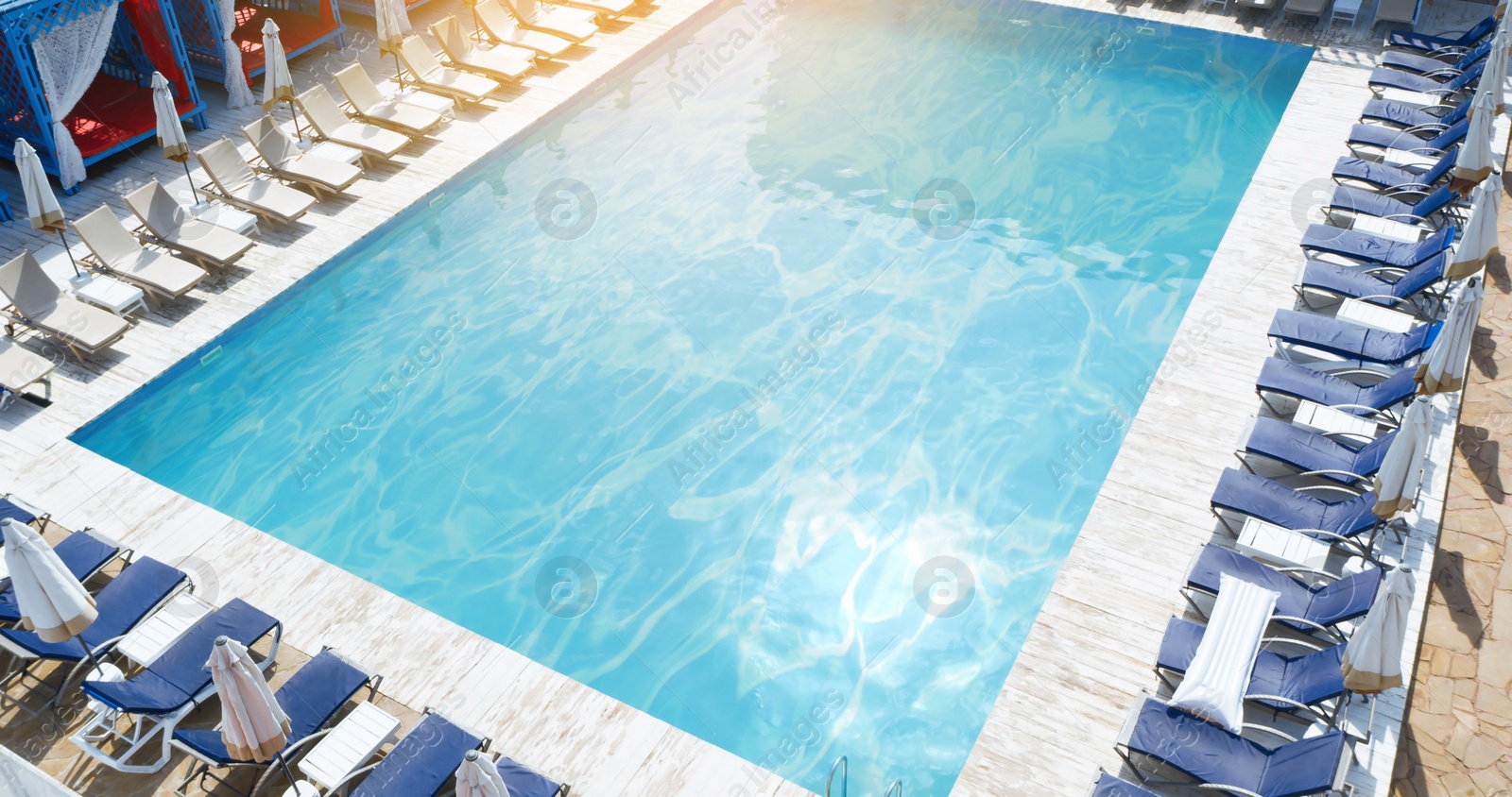 Image of Lounge chairs with umbrellas near swimming pool on sunny day 