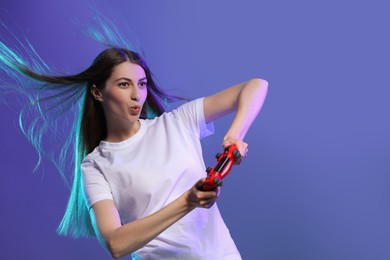 Excited woman playing video games with controller on violet background, space for text