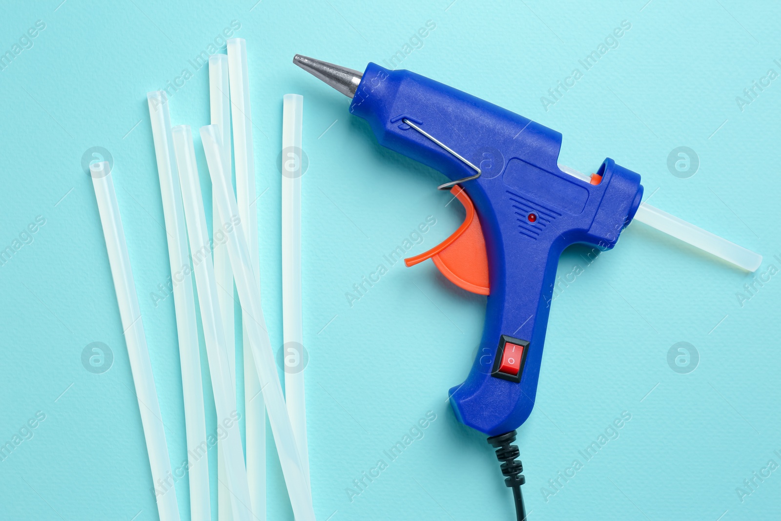 Photo of Blue glue gun and sticks on turquoise background, flat lay