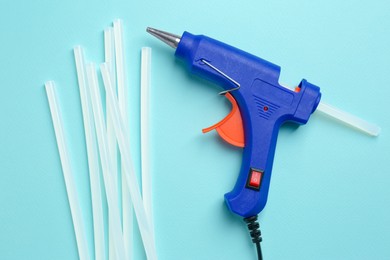 Blue glue gun and sticks on turquoise background, flat lay