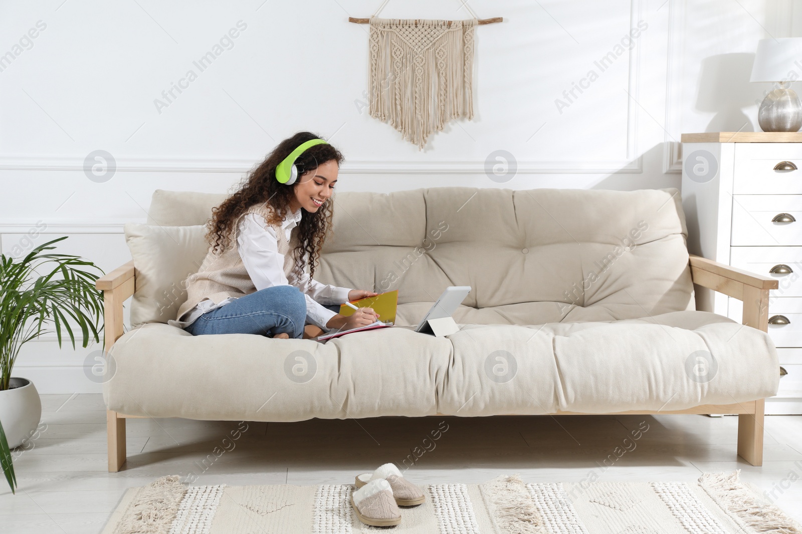 Photo of African American woman with headphones and tablet studying on sofa at home. Distance learning