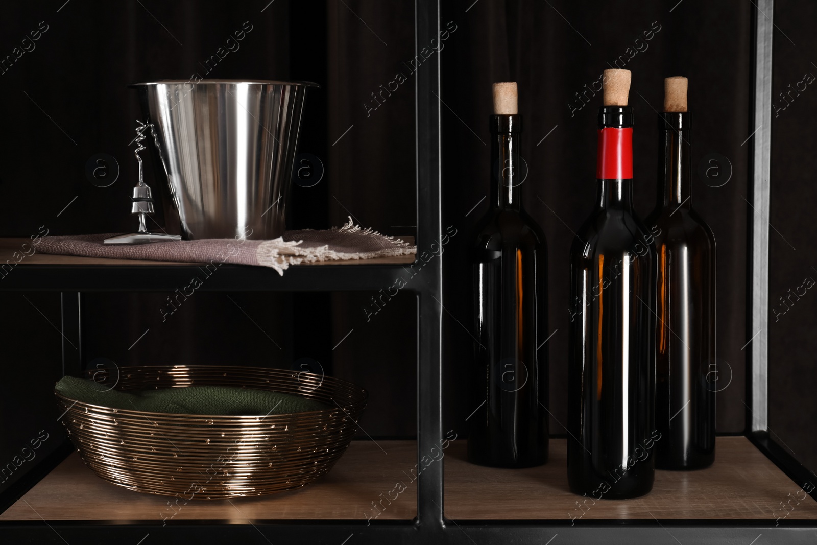 Photo of Bottles of wine, bucket and corkscrew on rack against black background