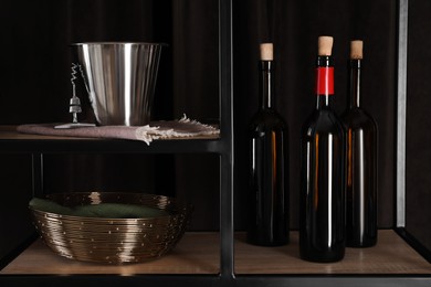 Photo of Bottles of wine, bucket and corkscrew on rack against black background