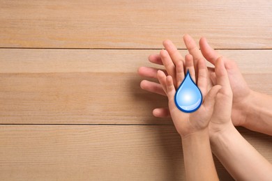 Family holding paper water drop on wooden background, top view. Space for text