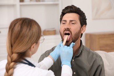 Photo of Doctor examining man`s oral cavity with tongue depressor indoors