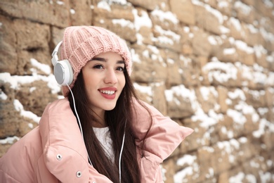Photo of Young woman listening to music with headphones against stone wall. Space for text