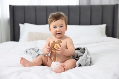 Cute baby boy with blanket and rattle sitting on bed at home