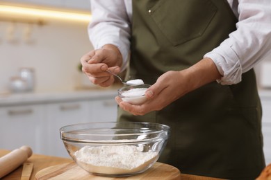 Photo of Making bread. Man putting salt into bowl with flour at wooden table in kitchen, closeup