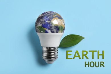 Image of Take care of environment. Light bulb with globe, green leaf and words Earth hour on light blue background, top view