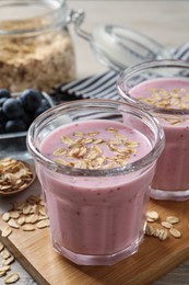 Photo of Glasses of tasty blueberry smoothie with oatmeal on wooden board, closeup