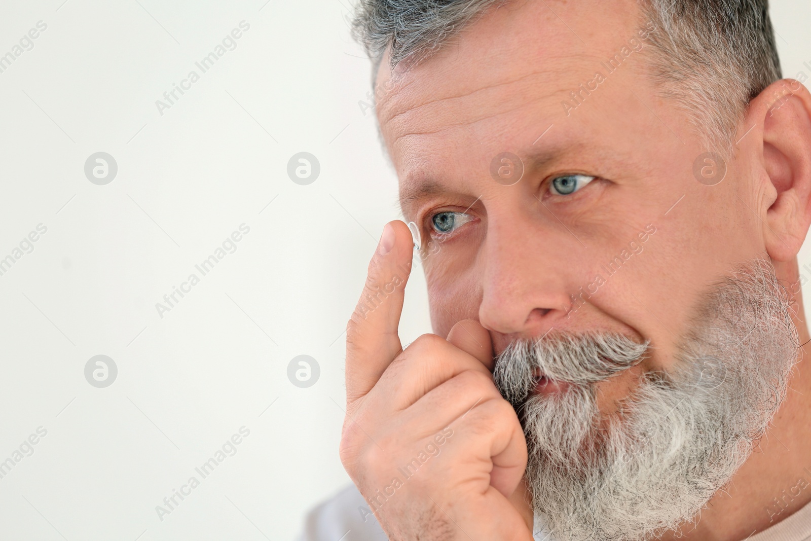 Photo of Senior man putting contact lens in his eye on light background