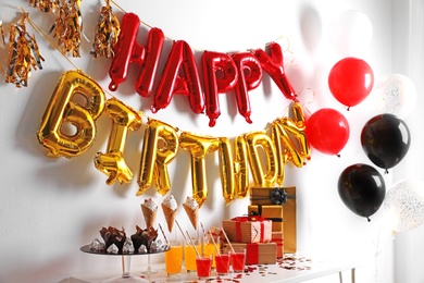 Treats and gifts on table in room decorated for birthday party with different balloons