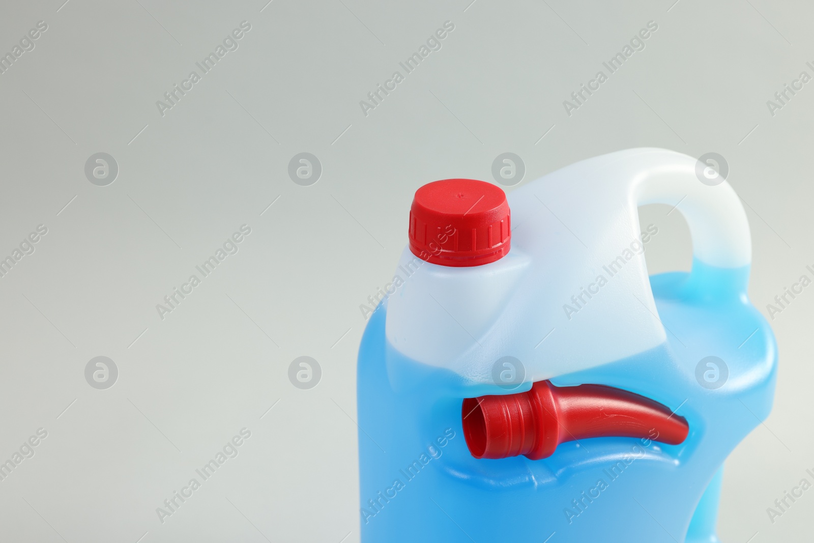 Photo of Plastic canister with nozzle and blue liquid on light grey background, closeup. Space for text