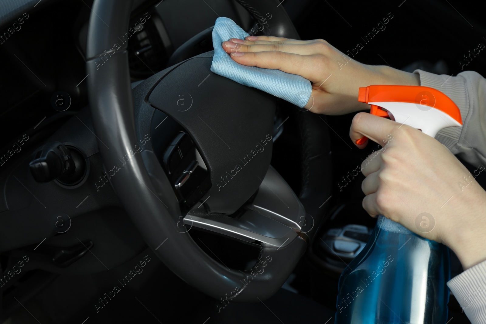 Photo of Woman cleaning steering wheel with rag in car, closeup