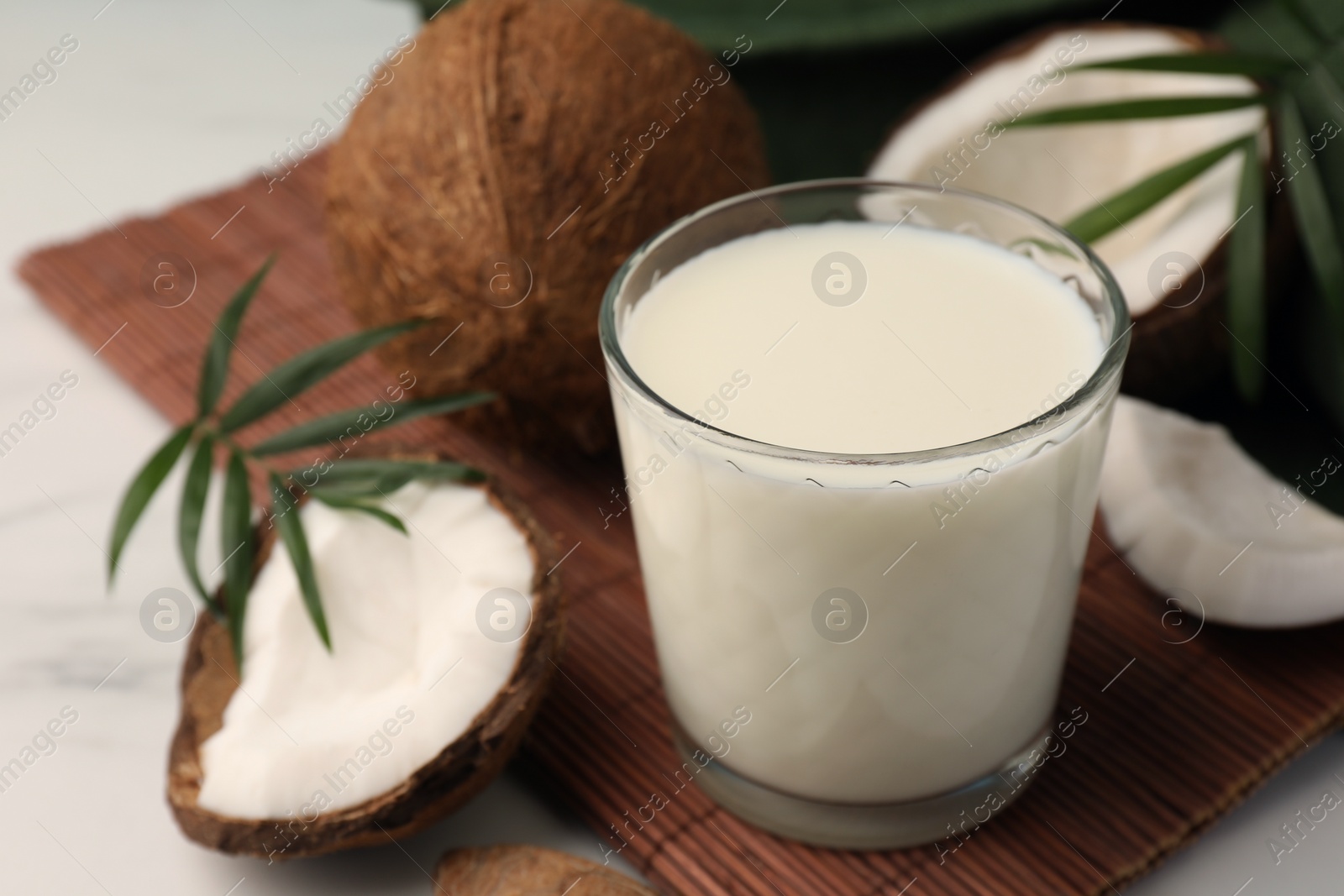 Photo of Glass of delicious vegan milk, coconut pieces and palm leaves on white marble table