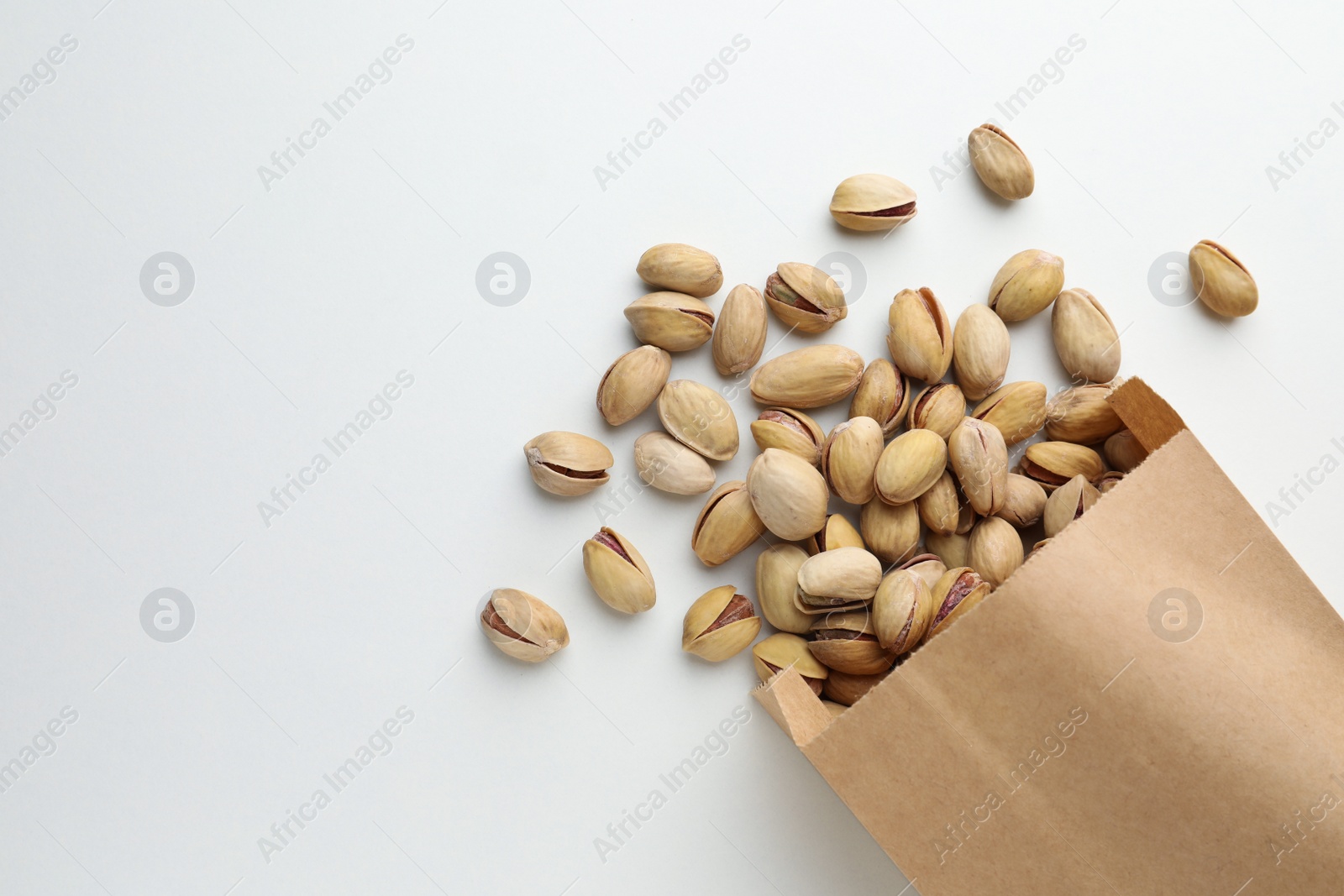 Photo of Overturned paper bag with pistachio nuts on white background, flat lay. Space for text