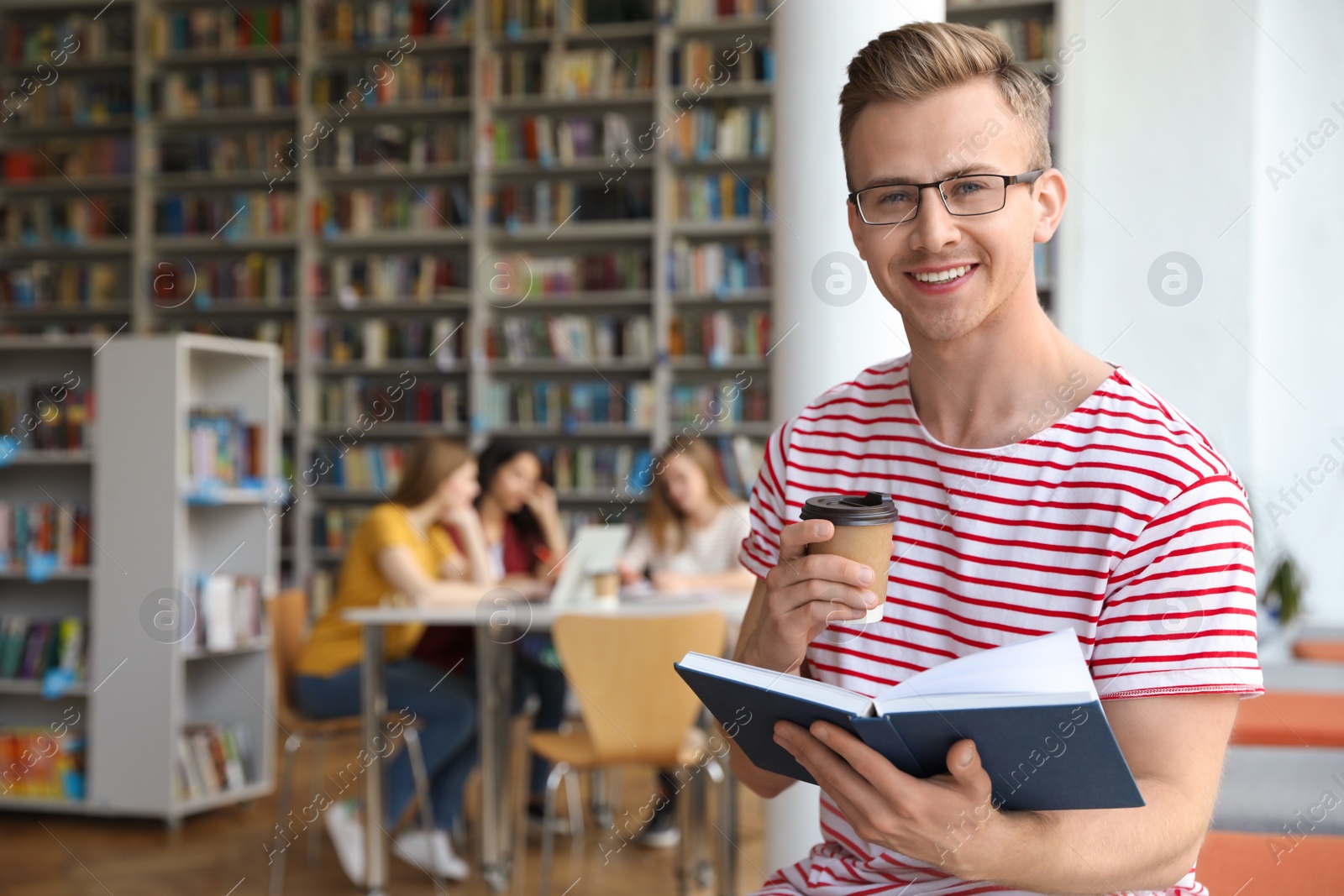 Photo of Young man with book and drink in library. Space for text