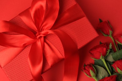 Photo of Beautiful gift box with bow and roses on red background, flat lay