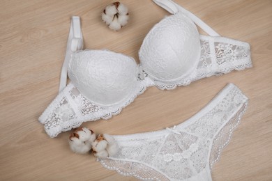 Photo of Elegant white women's underwear and cotton flowers on wooden background, flat lay