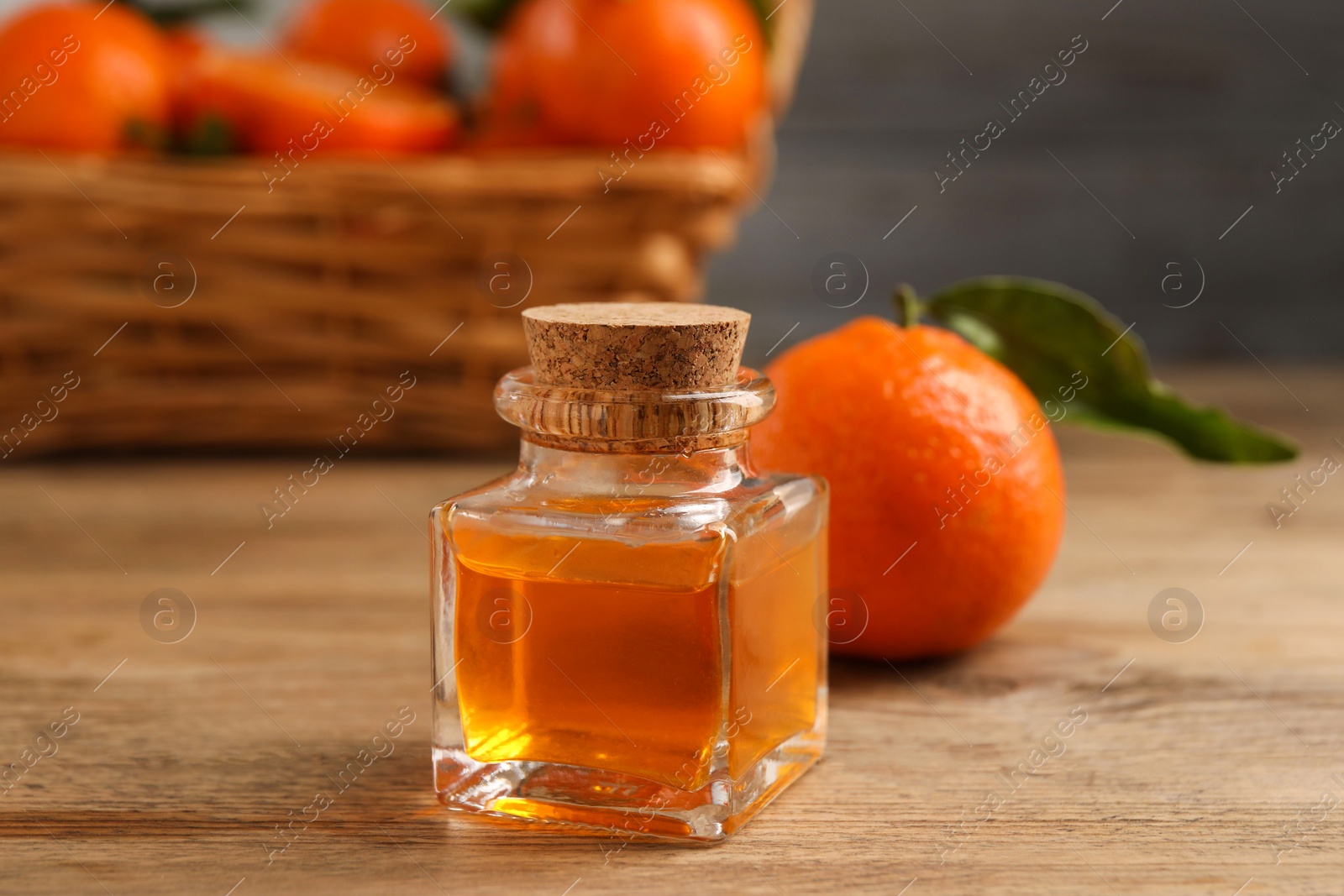 Photo of Bottle of tangerine essential oil and fresh fruit on wooden table, closeup