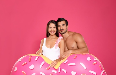 Young attractive couple in beachwear with inflatable ring on pink background