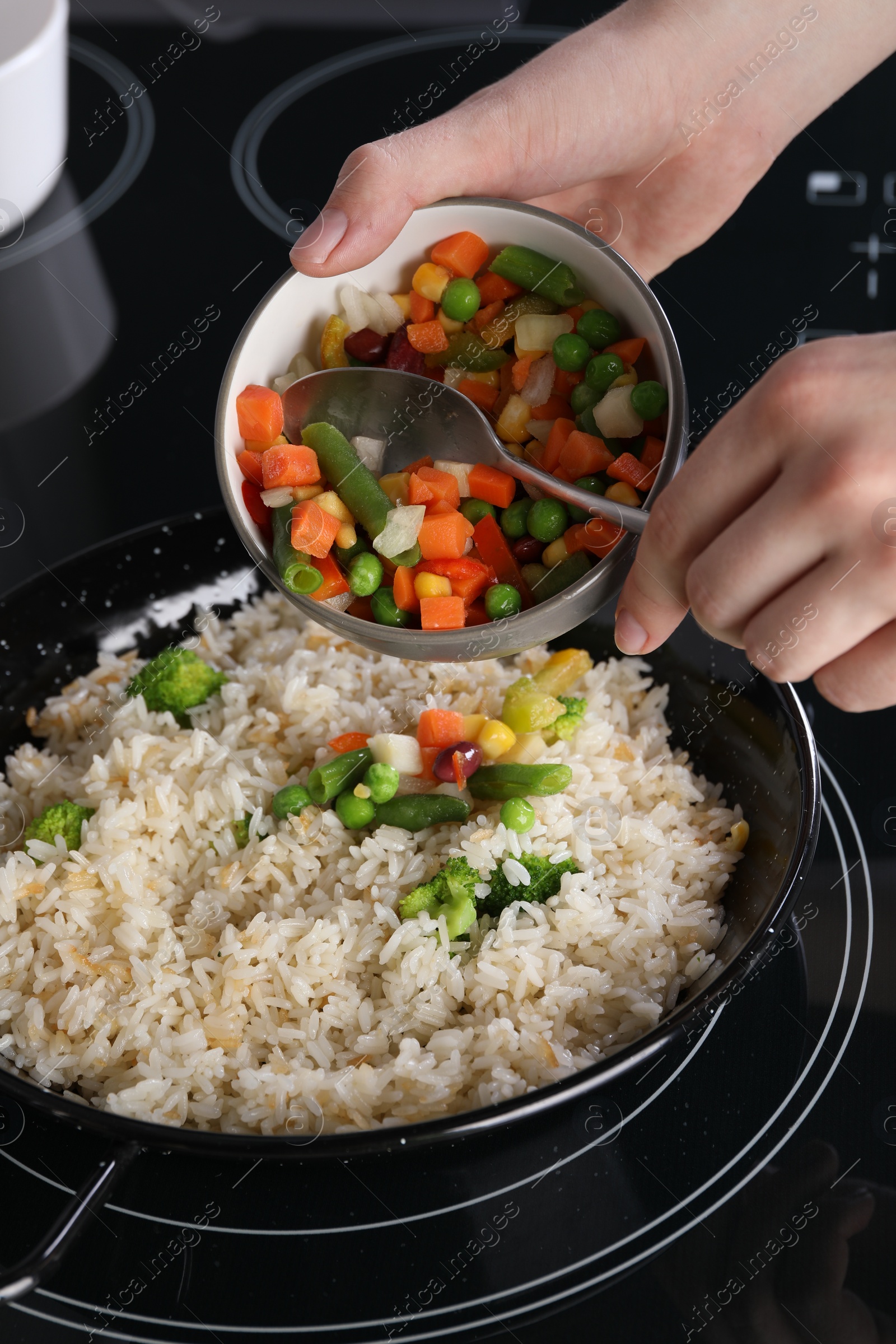 Photo of Woman cooking tasty rice with vegetables on induction stove, closeup