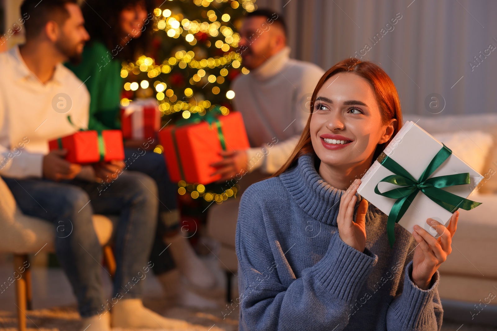 Photo of Christmas celebration in circle of friends. Happy young woman with gift box at home, selective focus