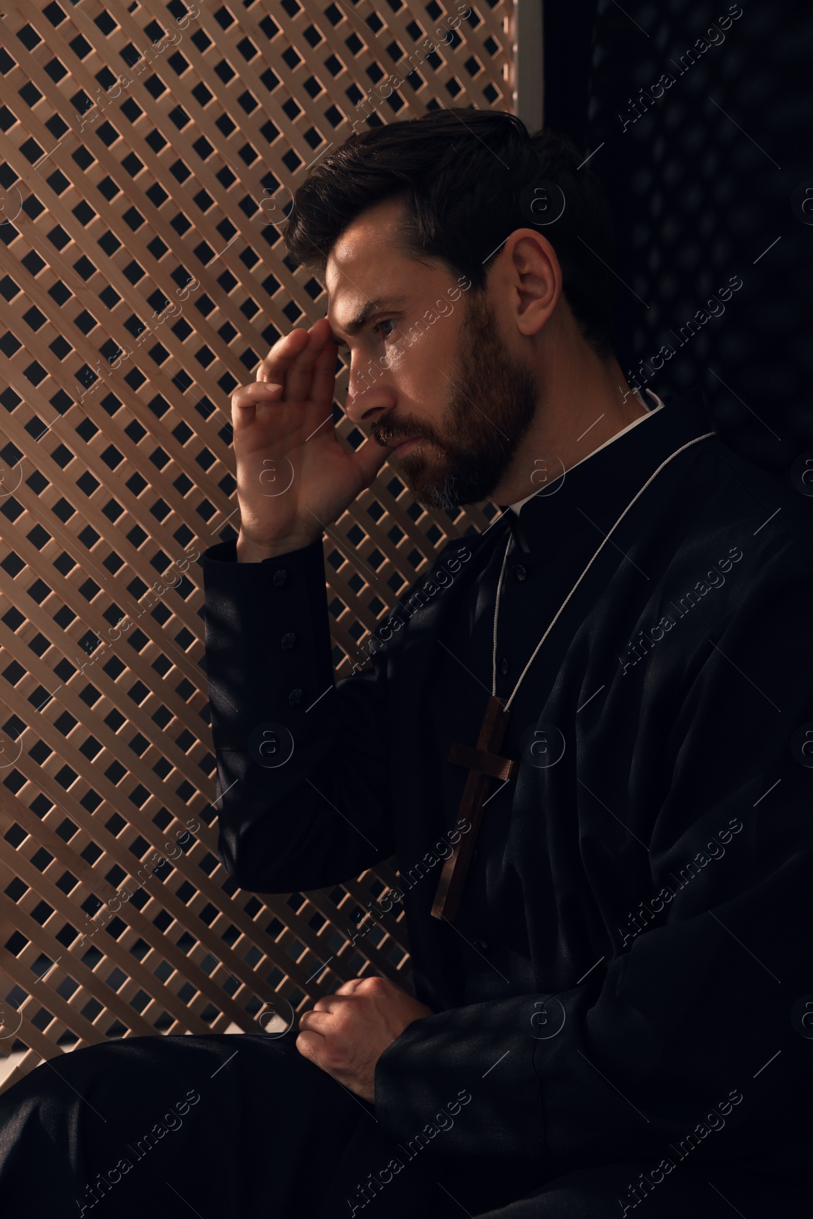 Photo of Catholic priest wearing cassock in confessional booth