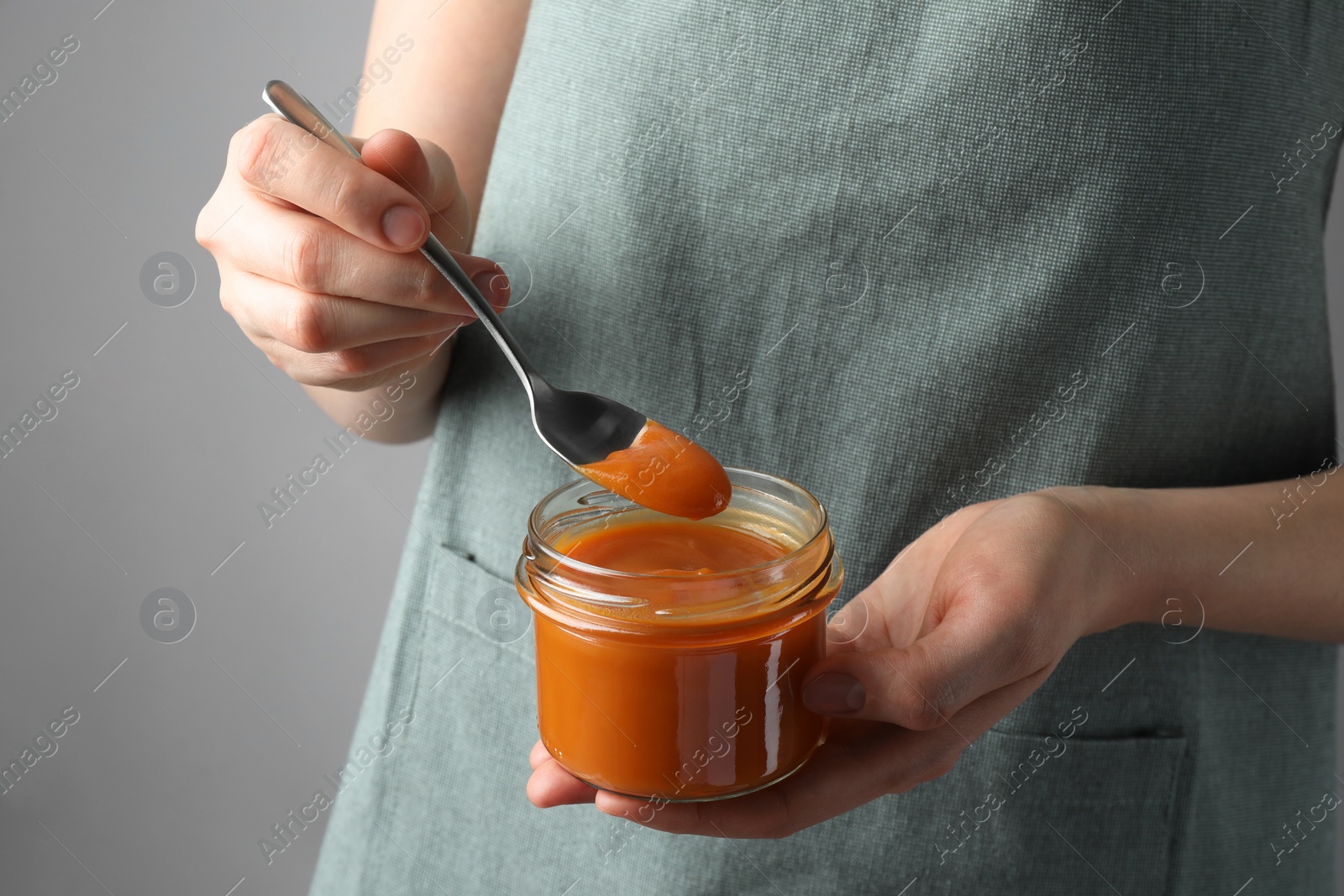 Photo of Woman with delicious persimmon jam on gray background, closeup