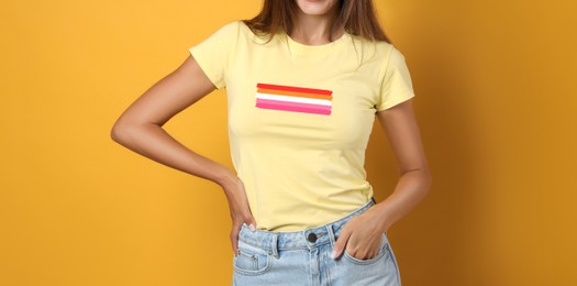 Image of Young woman wearing yellow t-shirt with lesbian flag on orange background, banner design. LGBT concept