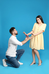 Photo of Young woman rejecting engagement ring from boyfriend on blue background