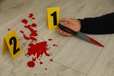 Photo of Crime scene markers and dead body with bloody knife on floor, closeup