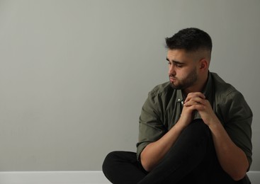 Sad man sitting near light grey wall. Space for text