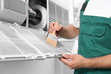 Photo of Professional male technician cleaning air conditioner indoors, closeup. Repair and maintenance