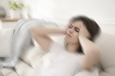 Image of Young woman suffering from migraine on sofa at home