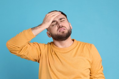 Man suffering from migraine on light blue background