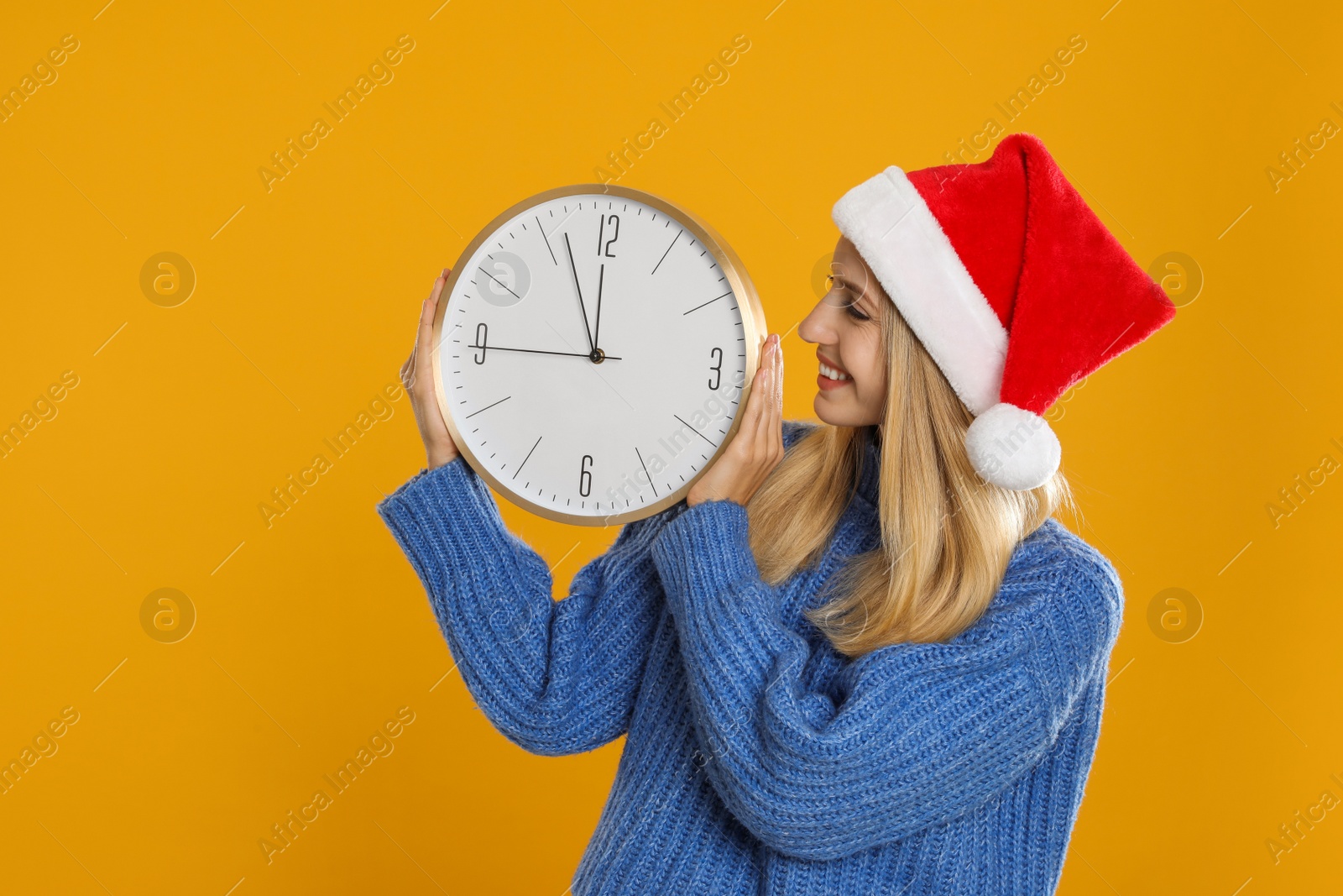 Photo of Woman in Santa hat with clock on yellow background. New Year countdown