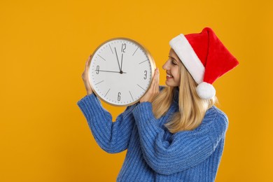 Photo of Woman in Santa hat with clock on yellow background. New Year countdown