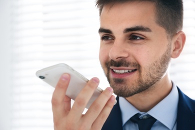 Photo of Young man using voice search on smartphone indoors, closeup