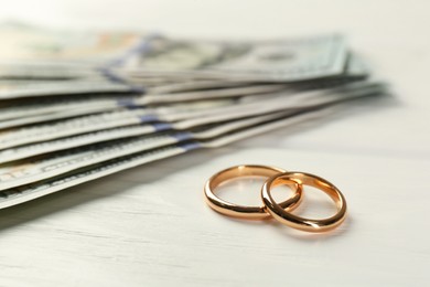 Honeymoon concept. Dollar banknotes and golden rings on white wooden table, closeup
