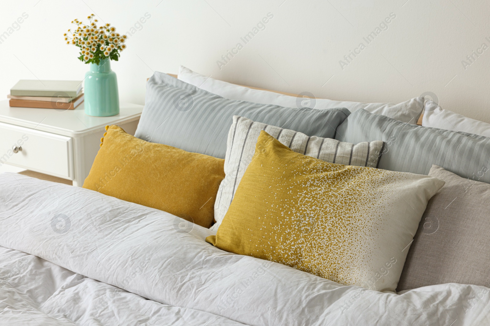 Photo of Beautiful room interior with comfortable bed and bouquet of chamomile flowers