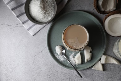 Photo of Glass of coffee with coconut milk, pieces and flakes on light grey table, flat lay. Space for text