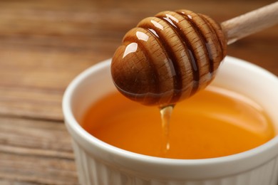 Pouring tasty honey from dipper into bowl on wooden table, closeup. Space for text