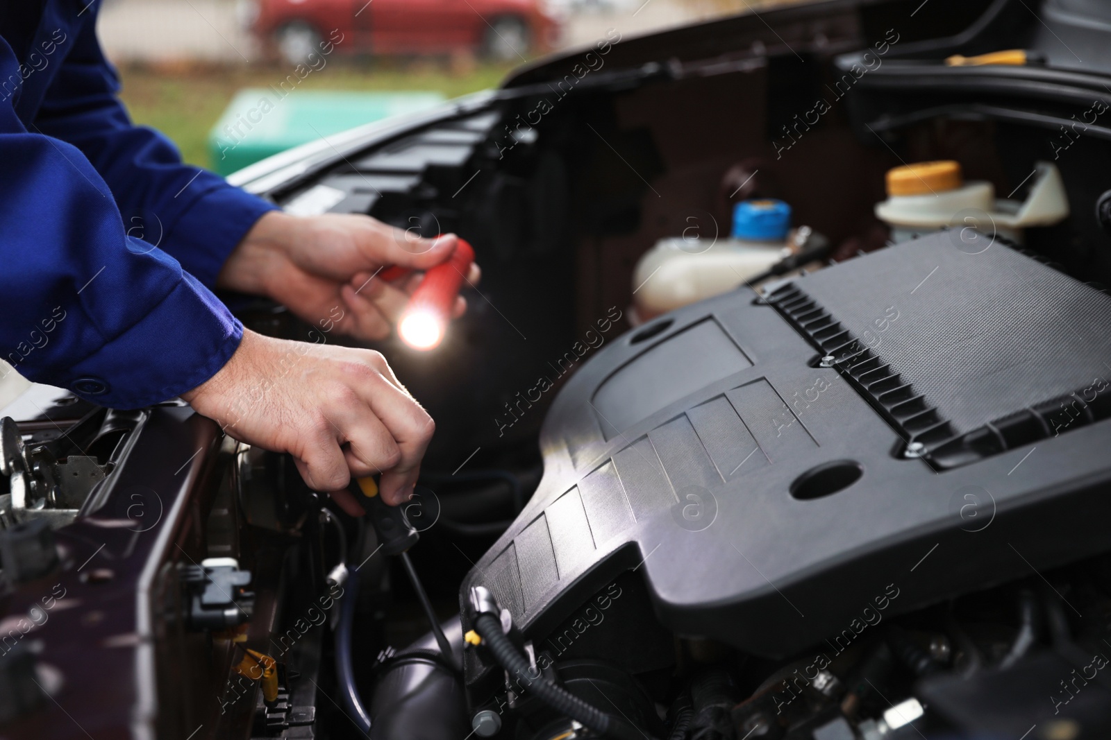 Photo of Mechanic with flashlight fixing car outdoors, closeup