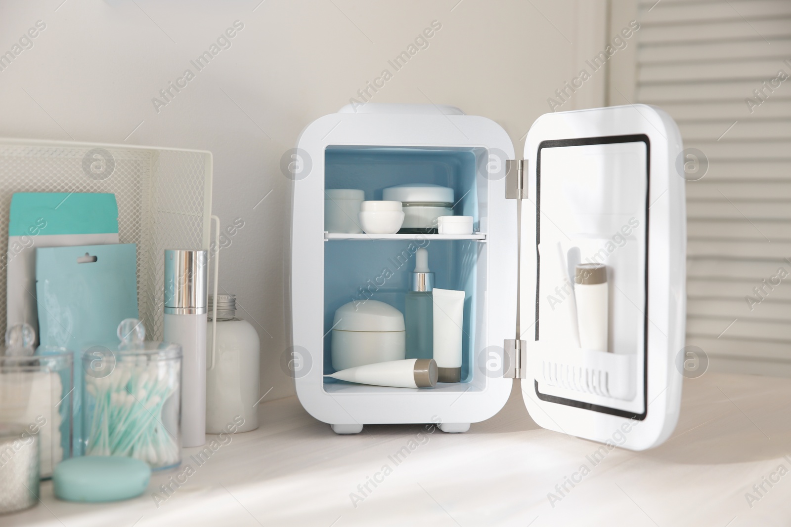 Photo of Cosmetics refrigerator and skin care products on white vanity table indoors