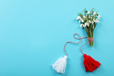 Photo of Beautiful snowdrops with traditional martisor on light blue background, flat lay and space for text. Symbol of first spring day
