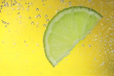 Photo of Juicy lime slice in soda water against yellow background, closeup